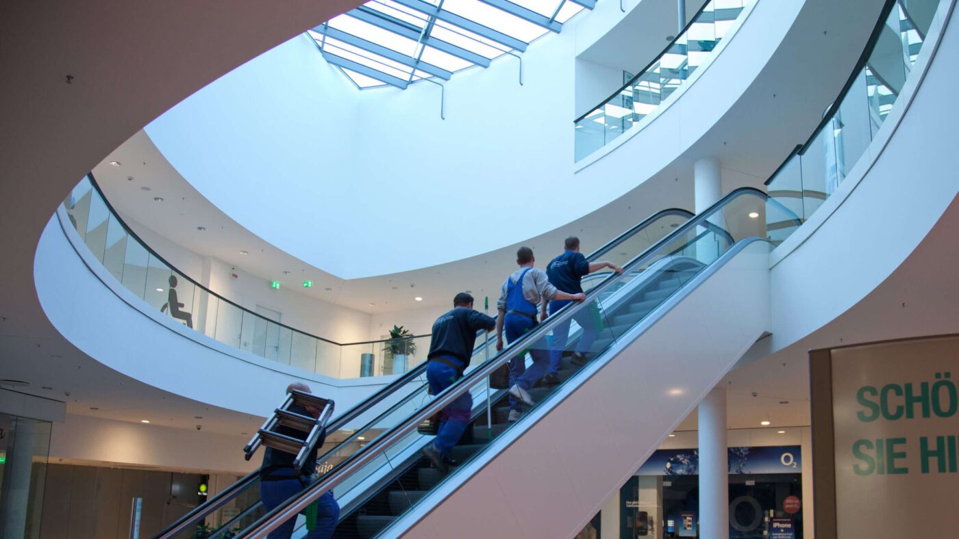 Gebäudereinigung Hannover | Mitarbeiter auf Rolltreppe in einem Einkaufszentrum auf dem Weg zur Reinigung